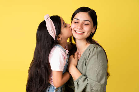 Adorable little girl kissing her beautiful mother on the cheek and sharing her happy feelings