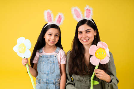 Portrait of a beautiful mother and young daughter wearing bunny ears and holding flowers for easterの写真素材