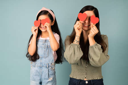 Family love. Adorable little girl and loving mother putting red hearts in front of their eyesの写真素材