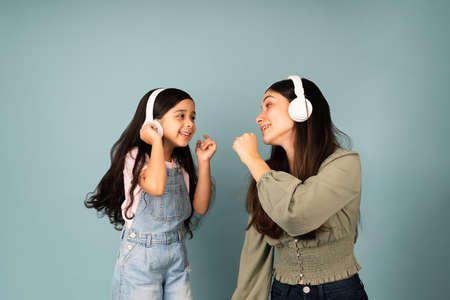 Sing with me. Hispanic young mom and little girl singing together while listening to music with headphonesの写真素材