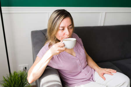 Slow mornings. Relaxed senior woman resting on the sofa and drinking a hot cup of coffee