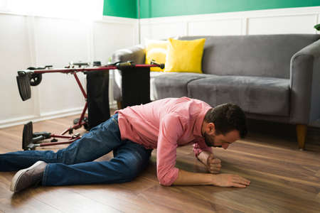 Disabled hispanic man having an accident. Paralyzed man falling down to the floor from his wheelchair while trying to move at homeの写真素材