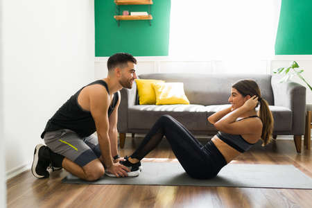 You can do it. Side view of a sporty woman doing crunches with the help of her happy boyfriend