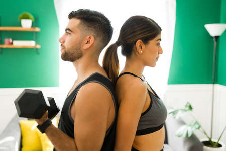 Profile of attractive workout partners in activewear doing bicep curls and lifting weights