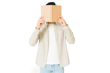 Smart young man covering his face with a book while focusing on reading and studyingの写真素材