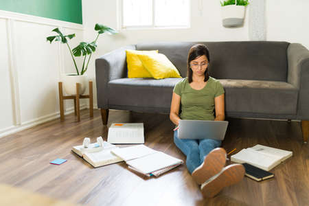 I'm ready for my exams. Smart young woman typing on the laptop while doing homework at home and studying for collegeの写真素材