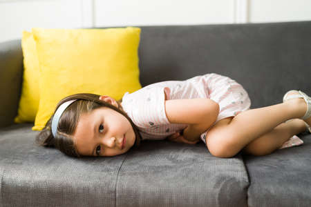 My stomach hurts. Pained young little girl feeling sick and suffering from stomachacheの写真素材
