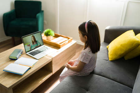 Rear view of an adorable little kid using a laptop and paying attention to her online teacher during her virtual class at homeの写真素材