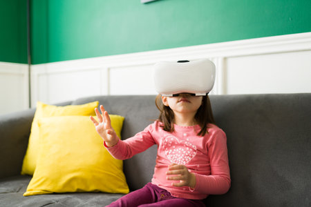 Caucasian little girl experiencing a virtual reality video game with a VR headset and playing at homeの写真素材