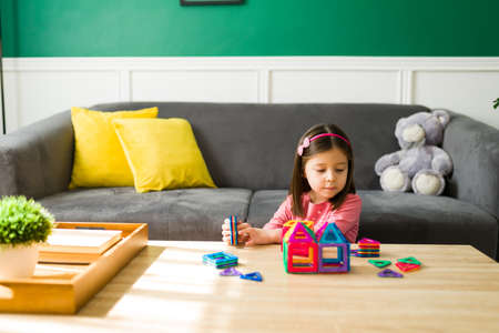 Elementary young kid playing a game with building blocks while sitting on the living roomの写真素材