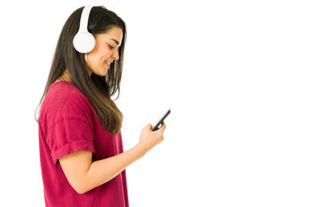 Profile of a beautiful young woman with headphones listening to music and texting on her phone