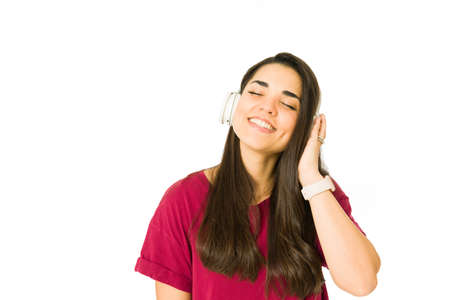 Relaxed woman with her eyes closed smiling while using wireless headphones and listening to relaxing musicの写真素材
