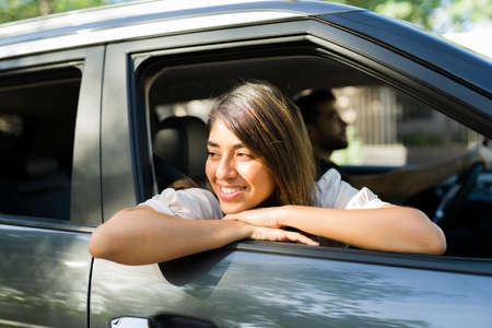 Carefree young woman looking out the car window and enjoying the view while driving during a road...