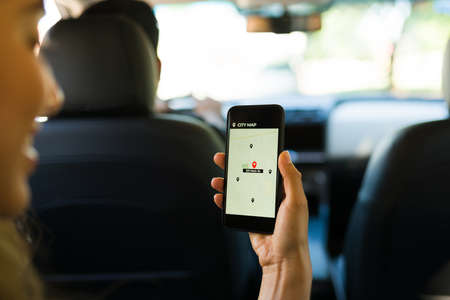 Close up of a female passenger looking at the GPS map on her smartphone while taking a ride on a carpool service appの写真素材