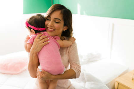 Loving family. Beautiful young mother smiling while hugging her newborn baby girl at home