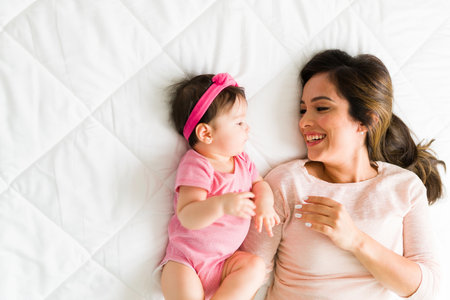 Top view of a happy mother and newborn baby girl resting in bed. Beautiful family relaxing in the...