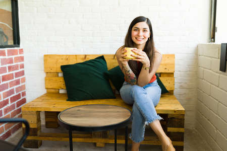 Cheerful young woman sitting alone outside at a hipster coffee shop and drinking a delicious coffee
