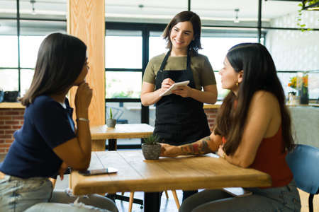 Happy waitress taking the order of the customers at the table. Women friends ordering food and drinks at the restaurantの写真素材