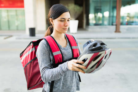 Attractive delivery girl taking off her safety helmet after getting down from the bicycle while delivering foodの写真素材