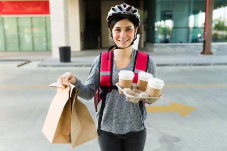 Happy delivery girl smiling while making eye contact with coffee to go and a lunch bag while delivering to a customerの写真素材