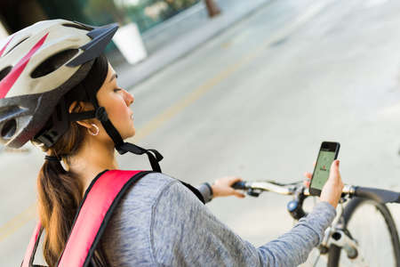 Hispanic delivery girl on a bike searching for the customer's address in the map to make a food delivery in the cityの写真素材