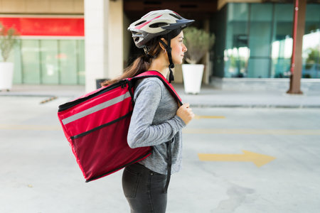 Profile of a latin young woman with a delivery backpack with food getting down from her bike in the cityの写真素材