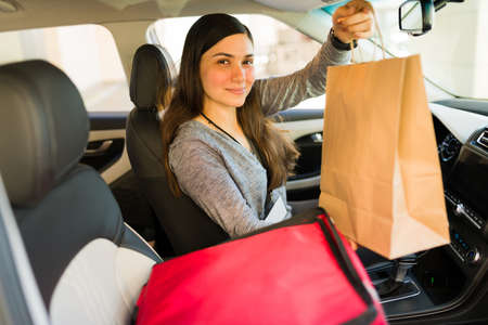 Gorgeous young woman delivering a food order to a customer in the carの写真素材
