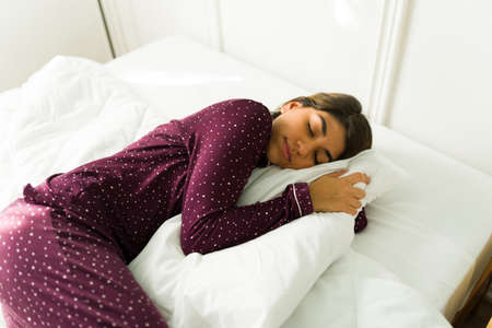 Relaxed young woman hugging a pillow and sleeping on a comfortable fresh bed while having beautiful...
