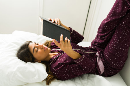 Gorgeous latin woman in pjs reading a new book while resting on the bed during the morningの写真素材