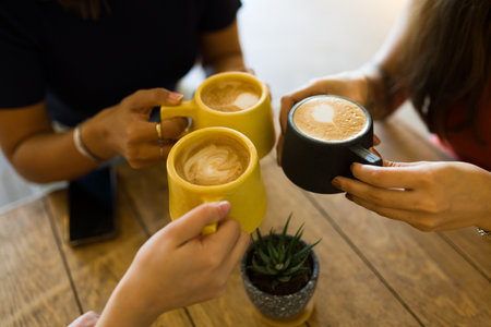 Close up of female hands making a toast and drinking delicious lattes and capuccinos at a restaurantの写真素材