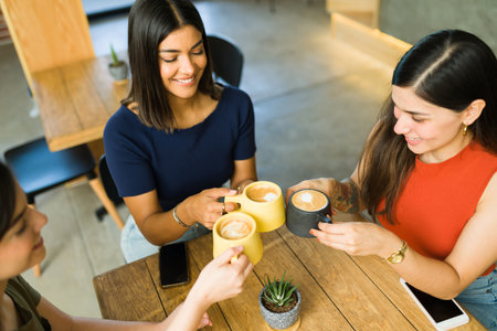 Top view of three happy best friends toasting with cups of coffee and laughing while enjoying a good conversationの写真素材