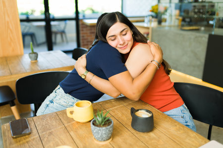 I love you so much. Lovely female friends hugging and smiling while sitting at a restaurant with a cup of coffeeの写真素材