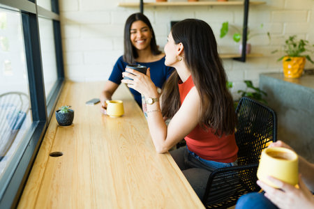 Cheerful young women and best friends drinking a cup of coffee while enjoying a fun conversationの写真素材