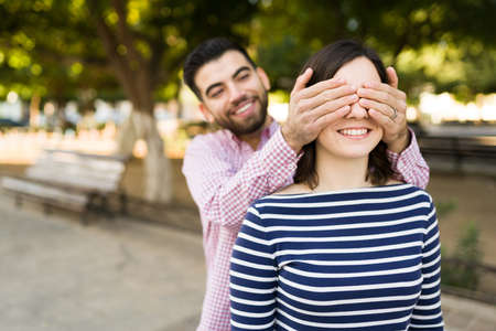 You miss me? Handsome young man covering her girlfriend's eyes and surprising her for a date outdoorsの写真素材