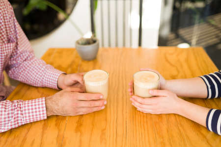 Close up of the hands of a couple holding cappuccinos at the coffee shop during a dateの写真素材