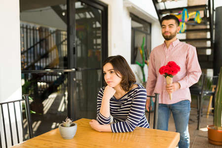 I'm sorry I'm late. Young man bringing flowers to her angry girlfriend waiting at a coffee shopの写真素材