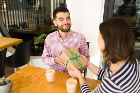 Cheerful handsome boyfriend receiving a birthday gift from her lovely girlfriend at the cafeの写真素材