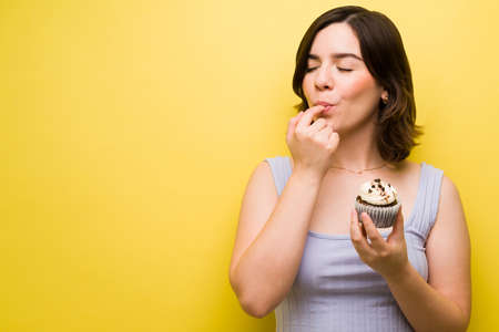 Sugar cravings. Young woman licking her lips and eating a chocolate cupcake with icingの写真素材