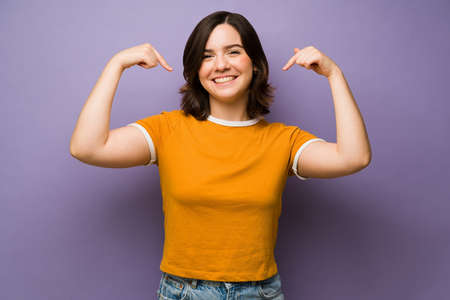 Beautiful woman smiling and pointing to her beaming smile in front of a studio purple backgroundの写真素材