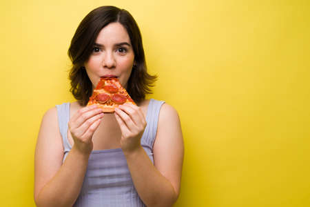 Attractive woman looking at the camera while eating a slice of delicious pizzaの写真素材