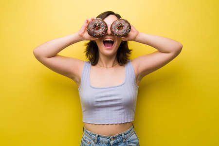 Fun caucasian woman holding chocolate donuts in front of her eyes and laughingの写真素材