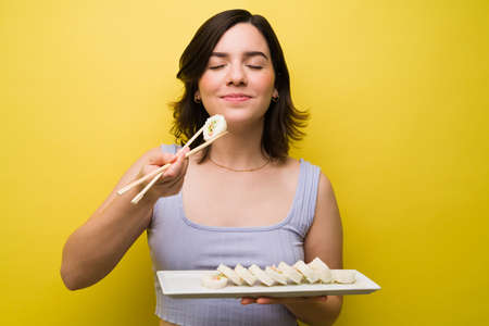 I love asian food. Gorgeous woman holding a sushi roll with chopsticks with her eyes closedの写真素材