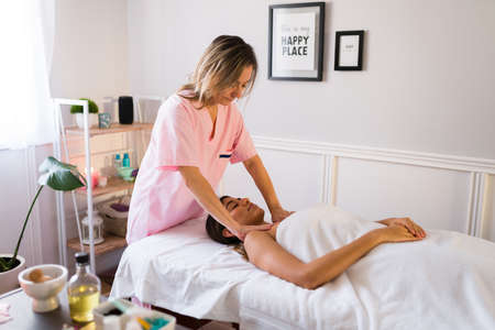 Professional therapist giving a shoulder massage to an hispanic relaxed woman at the beauty spaの写真素材