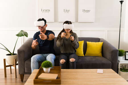 Cheerful fun couple laughing while using modern futuristic headsets and playing virtual reality video gamesの写真素材