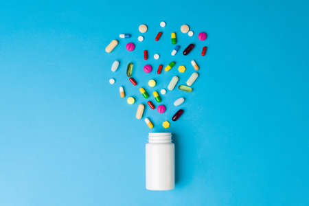 Health care is important. Flat lay of a white bottle of pills with a lot of colorful pills and...