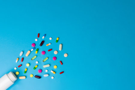 Colorful pills, capsules and drugs spilling from a white bottle of medicine on a blue background...