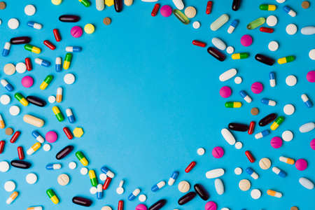 Studio shot of many colorful pills, antibiotics, painkillers and vitamins against a blue background with copy space text in a circleの写真素材