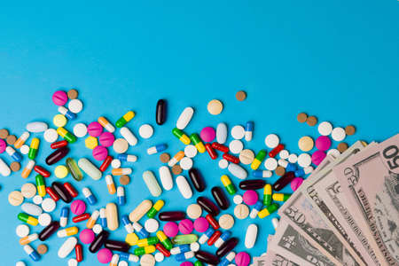 Health care cost. Assorted pills, drugs, pharmaceutical medicine and colorful vitamins against a background with money and copy spaceの写真素材