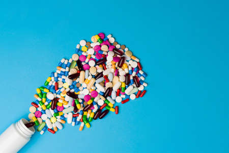 Drugs and medication. Flat lay of many assorted pills, capsules and tablets spilling out from a medicine bottleの写真素材