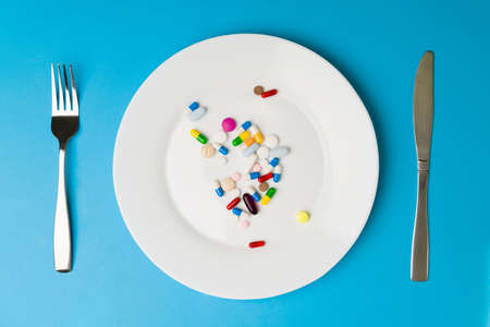 Unhealthy nutrition. Capsule vitamins and food supplements on a plate with a fork and a knifeの写真素材